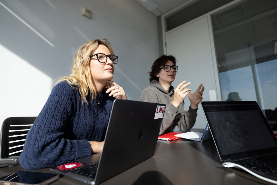 Two LMU students discuss a project while sitting in front of their computers.